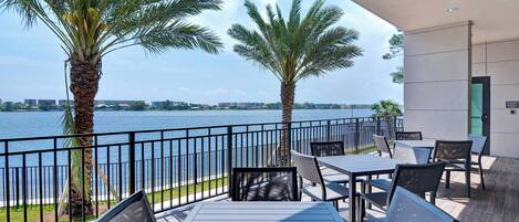 An outdoor terrace with a view of the water, palm trees, and modern furniture.