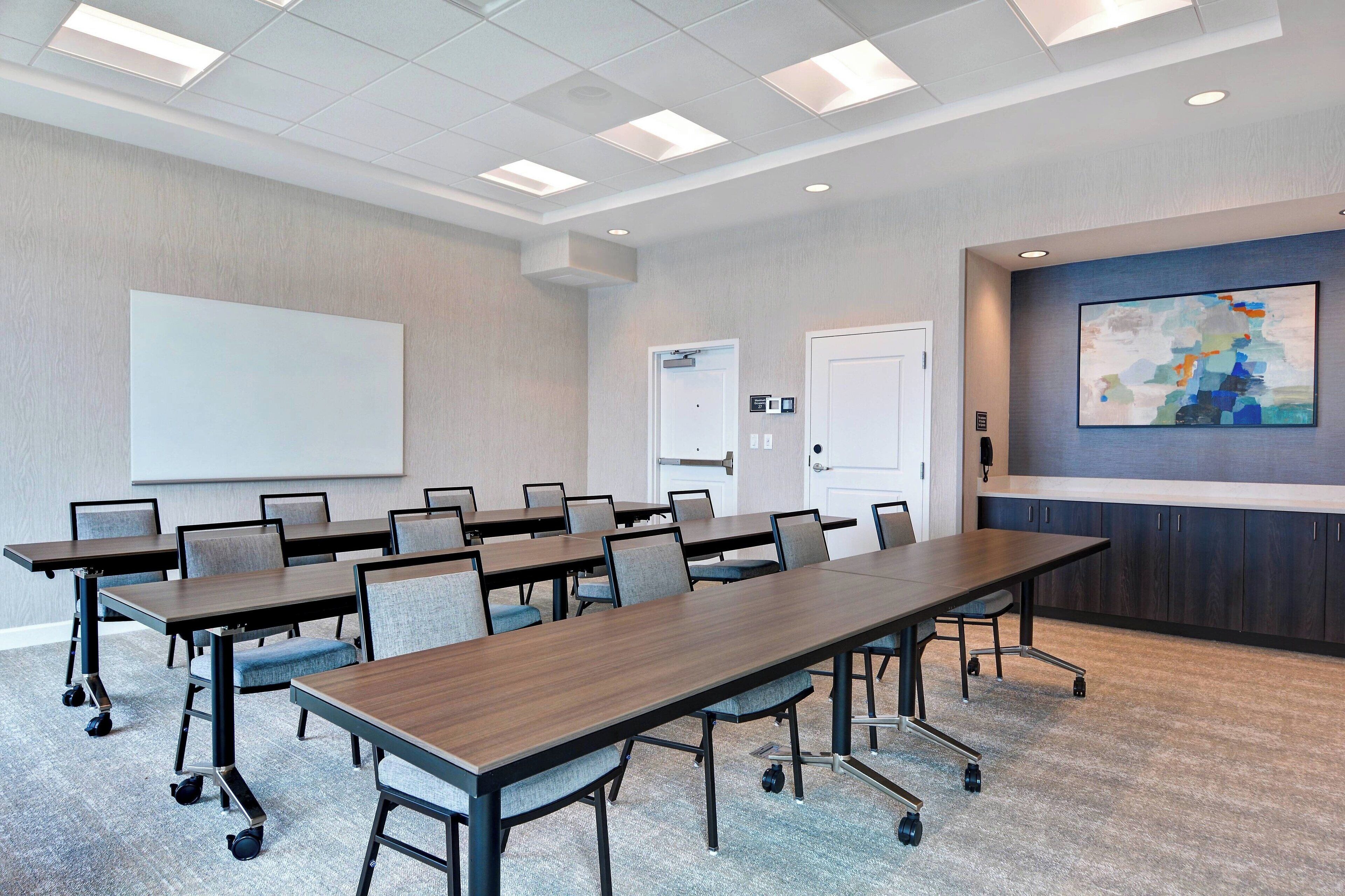 A conference room with a long table, chairs, a whiteboard, and a painting on the wall.