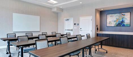 A conference room with a long table, chairs, a whiteboard, and a painting on the wall.