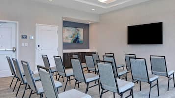 A conference room with a flat-screen TV, grey cushioned chairs, a white door, and a painting on the wall.