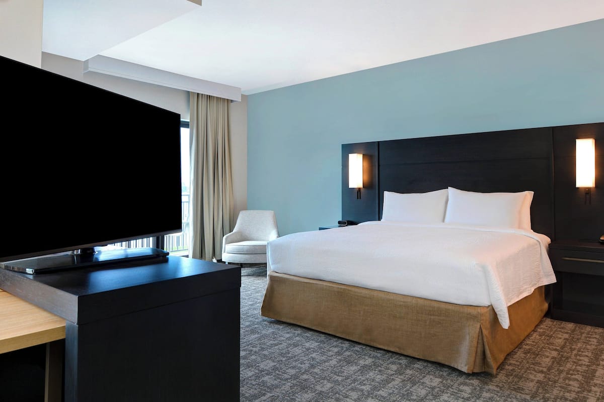 Ein Hotelzimmer mit einem großen Bett, einem Flachbildfernseher, einem Schreibtisch und einem Stuhl.
