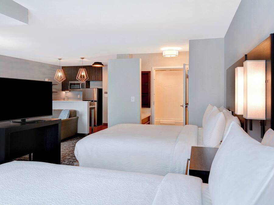 A hotel room with two beds, a TV, a desk, a microwave, and a kitchenette.