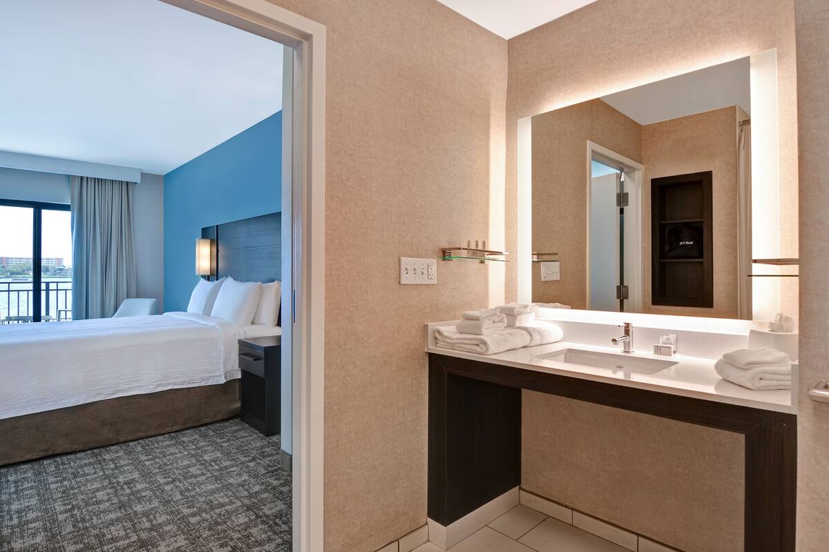Ein Hotelzimmer mit einem großen Bett, einem Badezimmer mit Waschbecken und Spiegel sowie Blick auf die Stadt.
