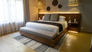 Une chambre moderne avec un grand lit, une tête de lit en bois, des tables de chevet et des œuvres d’art décoratives au mur.