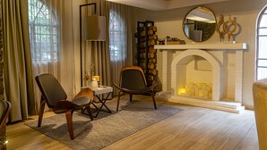 Un salon chaleureux avec une cheminée, deux fauteuils en cuir, une petite table avec une lampe et un miroir au-dessus du manteau de la cheminée.