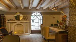 Une pièce chaleureuse avec une cheminée, des poutres en bois, un mur en pierre et une grande fenêtre.