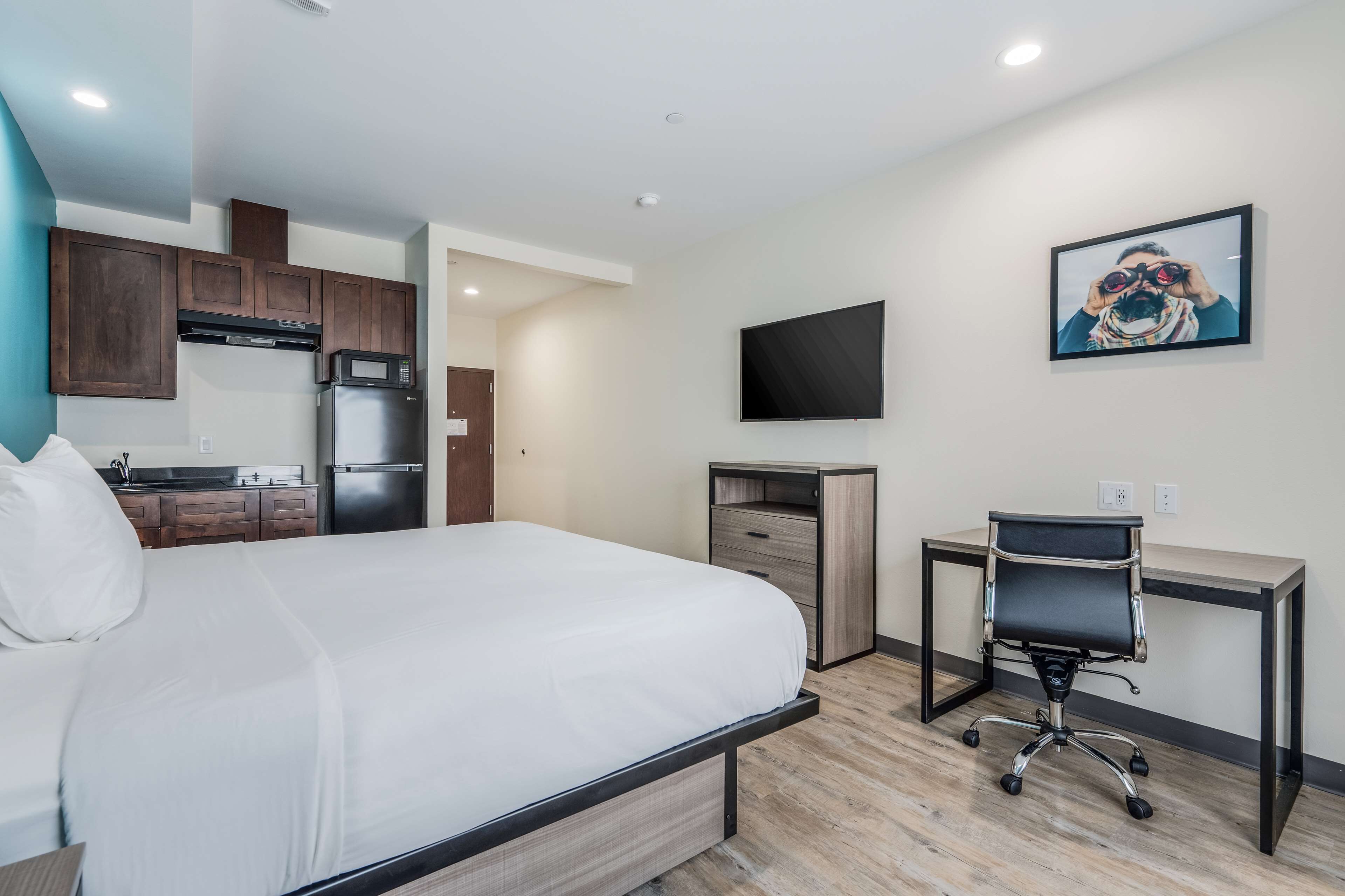 A hotel room with a bed, a desk, a chair, a television, and a kitchenette.