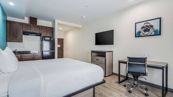 A hotel room with a bed, a desk, a chair, a television, and a kitchenette.