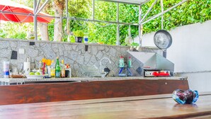 Uma área de cozinha externa com revestimento de pedra, diversos utensílios de cozinha e um suporte para panelas pendurado.