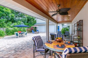 An outdoor patio with a round table, striped chairs, and a ceiling fan.