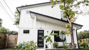 Una moderna casa a due piani con una porta d'ingresso nera, il numero 6201, e un piccolo giardino con un vialetto che conduce alla porta.