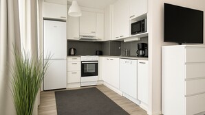 A modern kitchen with white cabinetry, a black microwave, a stove, and a coffee maker. - TH City Suite 1 (Tampere)