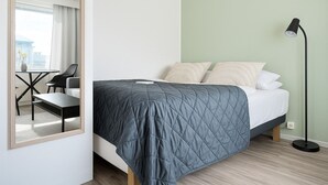 A bedroom with a bed, bedside lamp, and a view of a cityscape through a window. - TH City Suite 1 (Tampere)