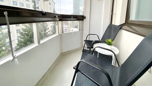 A balcony with a metal railing, two black chairs, a small table with a potted plant, and a view of buildings and trees. - TH City Suite 1 (Tampere)