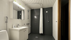 A modern bathroom with a toilet, sink, mirror, and shower area. - TH City Suite 1 (Tampere)