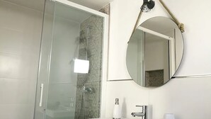 Een moderne badkamer met een douchecabine van glas, een witte wastafel, een ronde spiegel en een handdoek op het aanrecht.