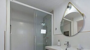Een moderne badkamer met een douchecabine van glas, een wastafel met spiegel en een houten vloer.