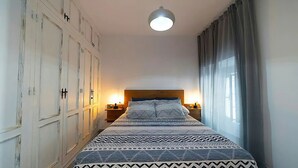 Een slaapkamer met een groot bed, een kledingkast en een nachtkastje met een lamp.