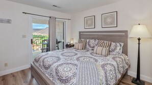 A bedroom with a large bed, a nightstand, a lamp, and a view of the outdoors.