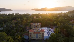 A multi-story building with a flat roof, surrounded by dense palm trees and a body of water in the background. - Walking Distance to Playa la Ropa  (Zihuatanejo)