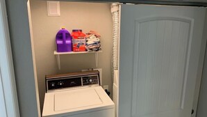 A laundry room with a washing machine, shelves with cleaning supplies, and a door. - DIA HideAway -2BR, 15 min from DIA DT, Anschutz MD (Commerce City)