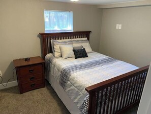 A bedroom with a bed, wooden nightstand, and a window with blinds.