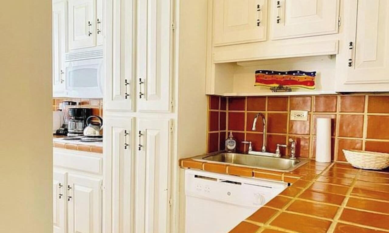 Une cuisine avec des meubles blancs, un pare-feu en carrelage, un lave-vaisselle et un évier.