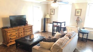 Ein Wohnzimmer mit einer Couch, einem Fernseher auf einer Holzkommode, einem Esstisch mit Stühlen und einem Deckenventilator.