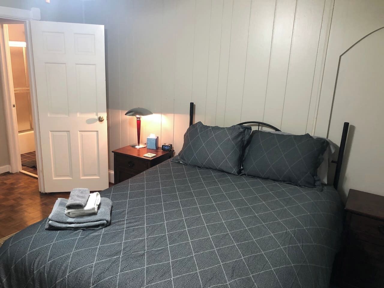 A bedroom with a bed, a nightstand, a lamp, and a door.