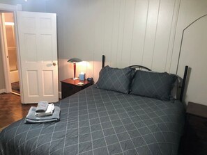 Ein Schlafzimmer mit Bett, Nachttisch, Lampe und einer Tür.