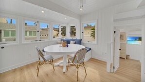 A bright, white room with a round table and chairs, a ceiling fan, and large windows offering a view of the outside.