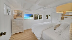 A bedroom with a bed, a dresser, a television, and a window with a view of the beach.