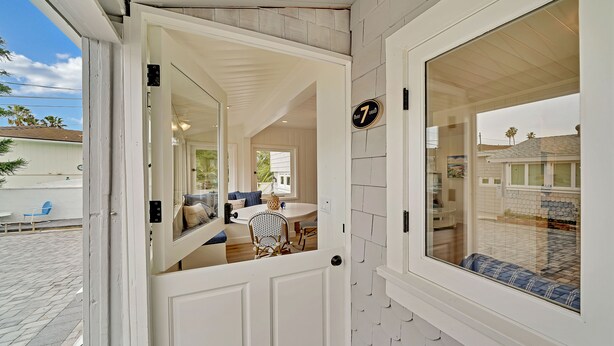 A white door with a number plate, a dining area with a table and chairs, and a view of the outside.