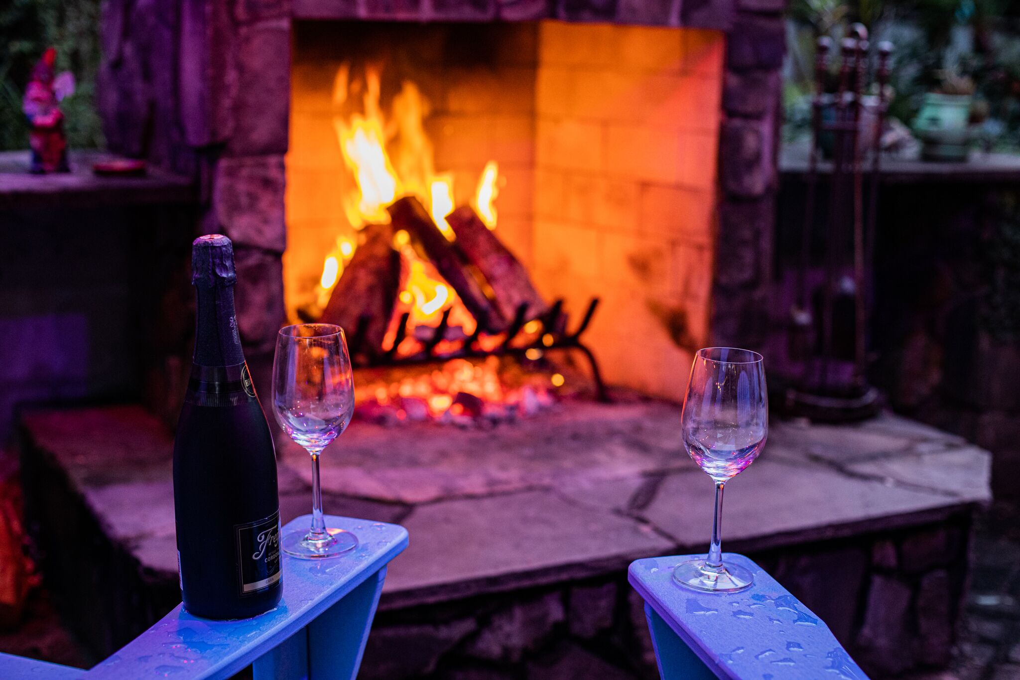 Une cheminée avec des bûches, deux verres et une bouteille posés sur une table en pierre.