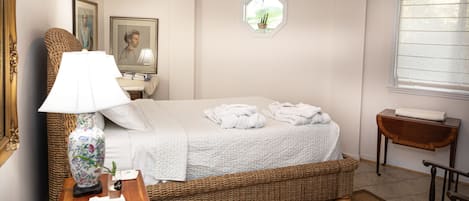 Un dormitorio ordenado con cama, lámpara de noche, cesta de mimbre y una mesita con lámpara.