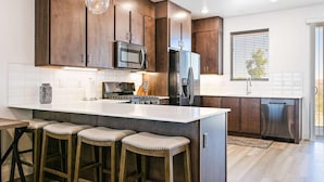 A modern kitchen with dark wood cabinets, stainless steel appliances, a large island with bar stools, and a window providing natural light. - Sunrise Corner #43 BEAUTIFUL RENTAL, GREAT LOCATION! (Saint George)