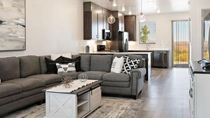 A modern living room with a gray sectional sofa, a white coffee table, and a kitchen with dark cabinets and stainless steel appliances. - Sunrise Corner #43 BEAUTIFUL RENTAL, GREAT LOCATION! (Saint George)