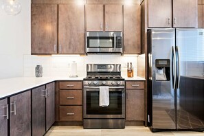 A modern kitchen with stainless steel appliances, wooden cabinets, and a white countertop.