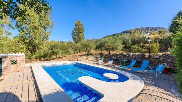 A rectangular swimming pool with a built-in jacuzzi, surrounded by a brick deck. There are blue lounge chairs and a small table with a lamp. - El Ranchito de Martín Álora by Ruralidays (Málaga)