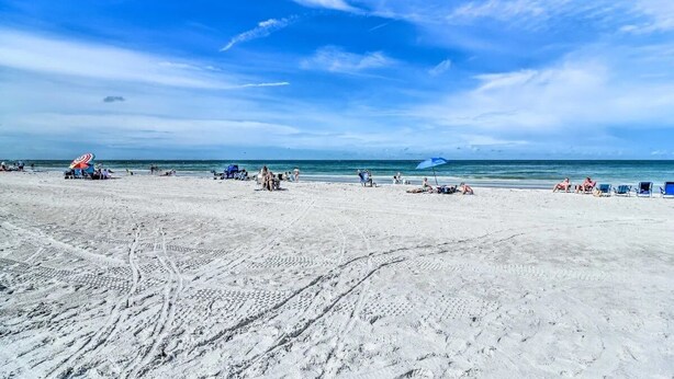 Ein sandiger Strand mit Fußabdrücken, einigen Personen und einem blauen Sonnenschirm.