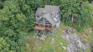 A two-story house with a porch, surrounded by dense forest.