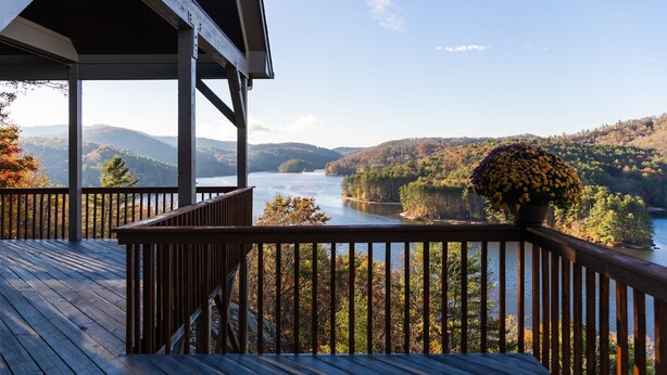 A wooden deck with a railing overlooking a lake surrounded by hills.