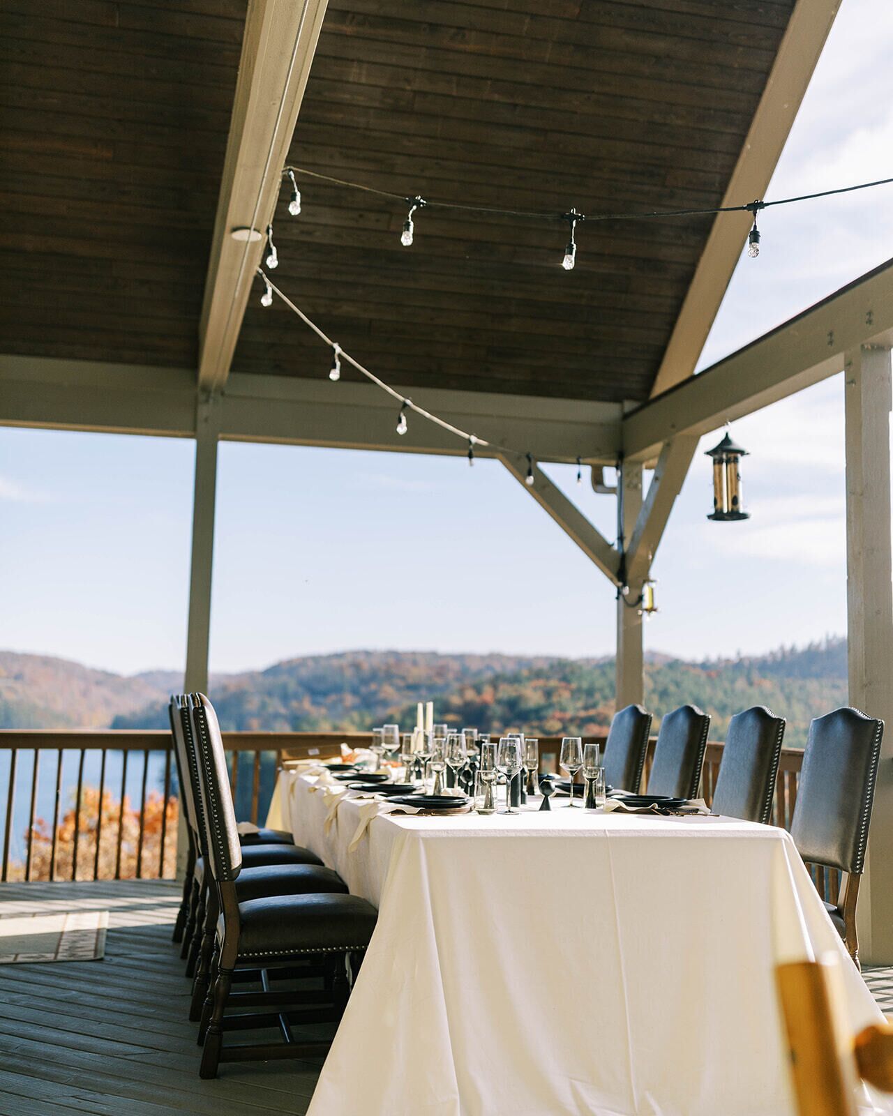 A dining table set for six with chairs, string lights, and a view of hills.