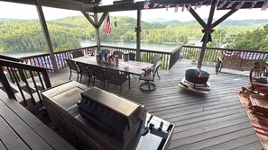 Una terraza con mesa y sillas, una parrilla y vistas a un lago y bosque.