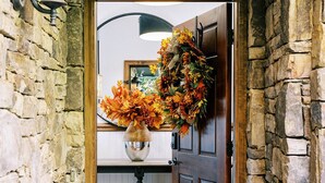 A stone-walled entrance with a wooden door, a welcome mat, and a floral wreath.