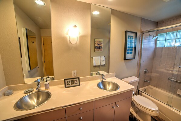 Een badkamer met twee wastafels, toilet, douche en een grote spiegel.