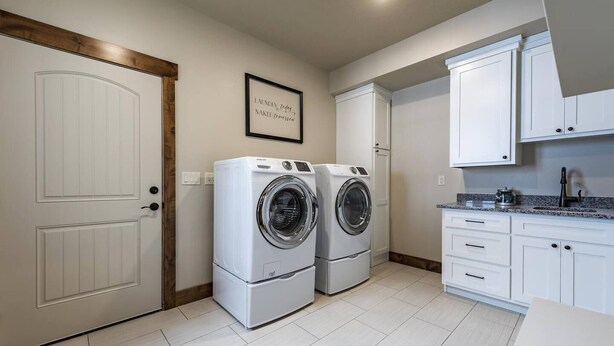 A laundry room with two front-loading washing machines, a white door, and a framed quote on the wall. - Luxury lakeview cabin w/hot tub, pool, sports courts, pickleball, private beach! (Fish Haven)