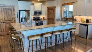 A modern kitchen with white cabinetry, a granite countertop, and a central island with bar stools. - Luxury lakeview cabin w/hot tub, pool, sports courts, pickleball, private beach! (Fish Haven)