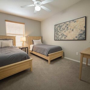 A bedroom with two beds, a ceiling fan, a window with blinds, a bedside table, a lamp, and a framed picture on the wall. - Across Chicago Cubs (Sloan Park) | Has Shared Pool (Tempe)