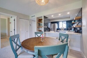 A modern kitchen with a round wooden table and teal chairs, a built-in oven, and a window overlooking the backyard.